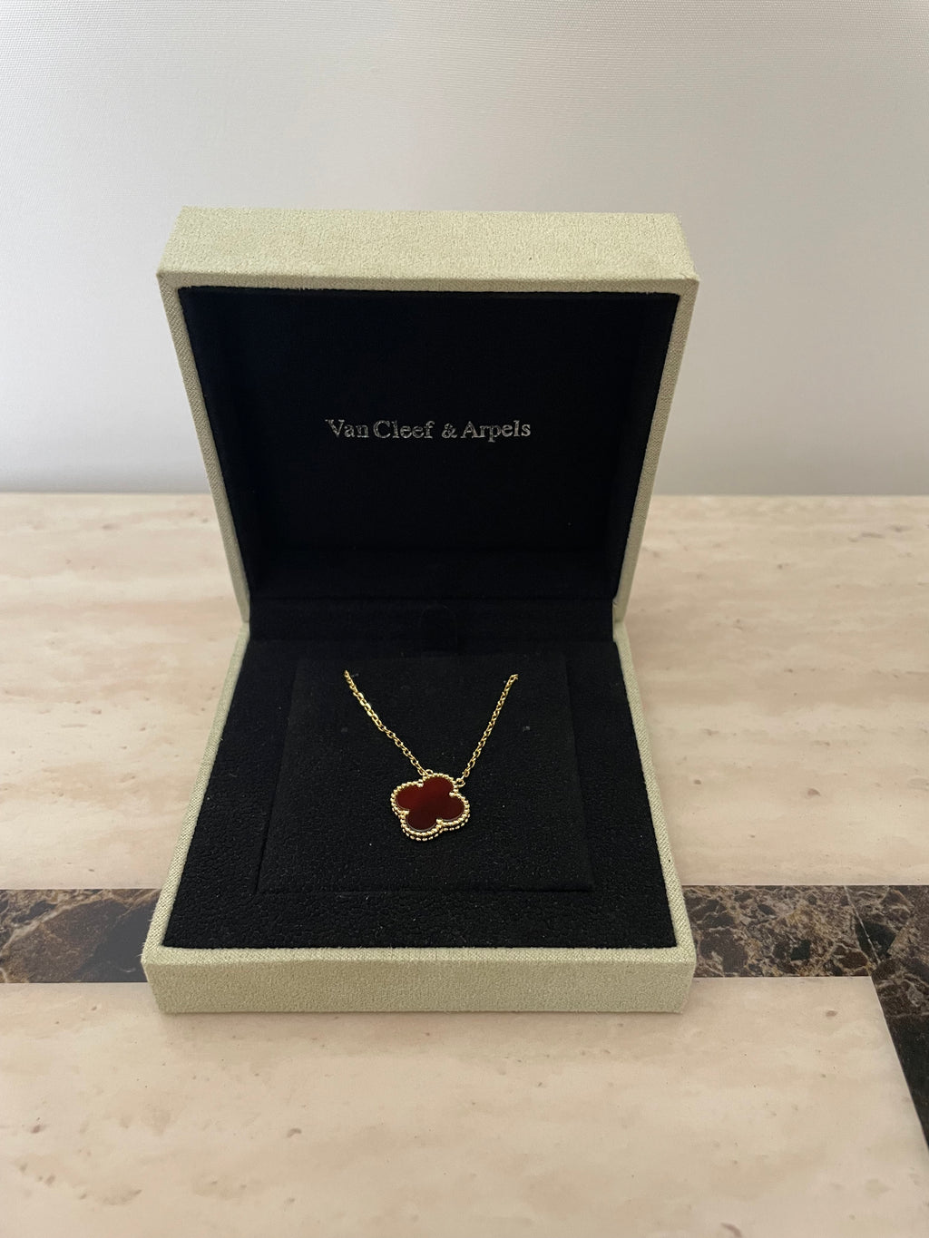 Open jewelry box with a necklace featuring a red stone on a textured surface.