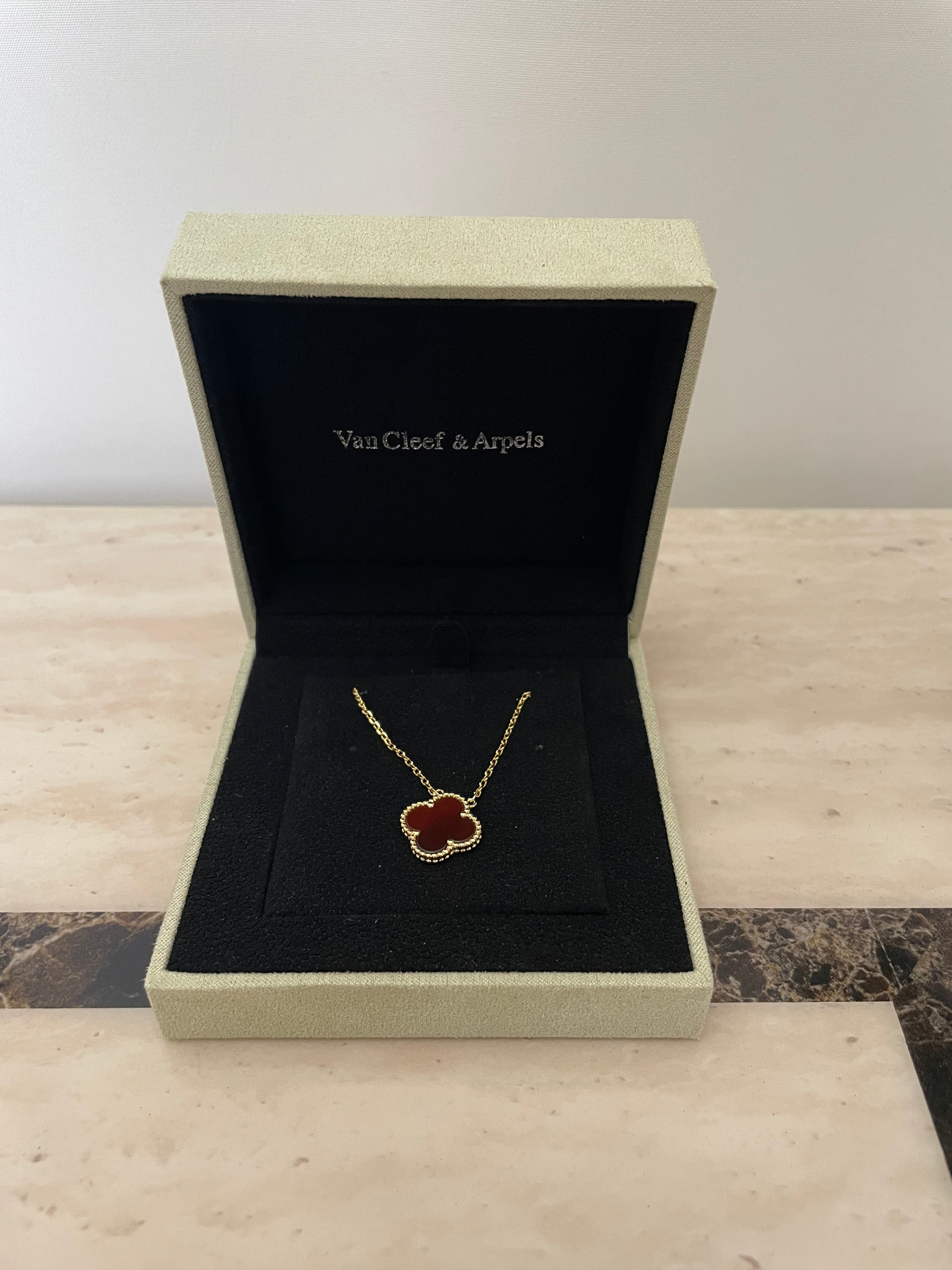 Open jewelry box with a necklace featuring a red stone on a textured surface.